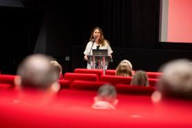 Adele Davidson speaking at a podium in the QFT theatre presenting to an audience sitting in red chairs